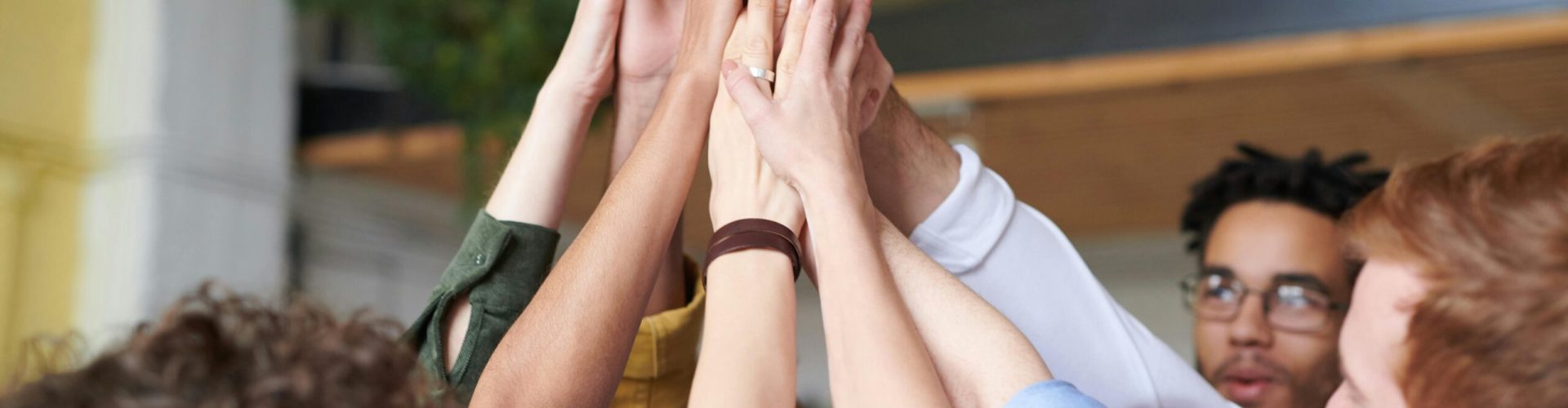A group of diverse professionals celebrating teamwork with a high-five indoors.